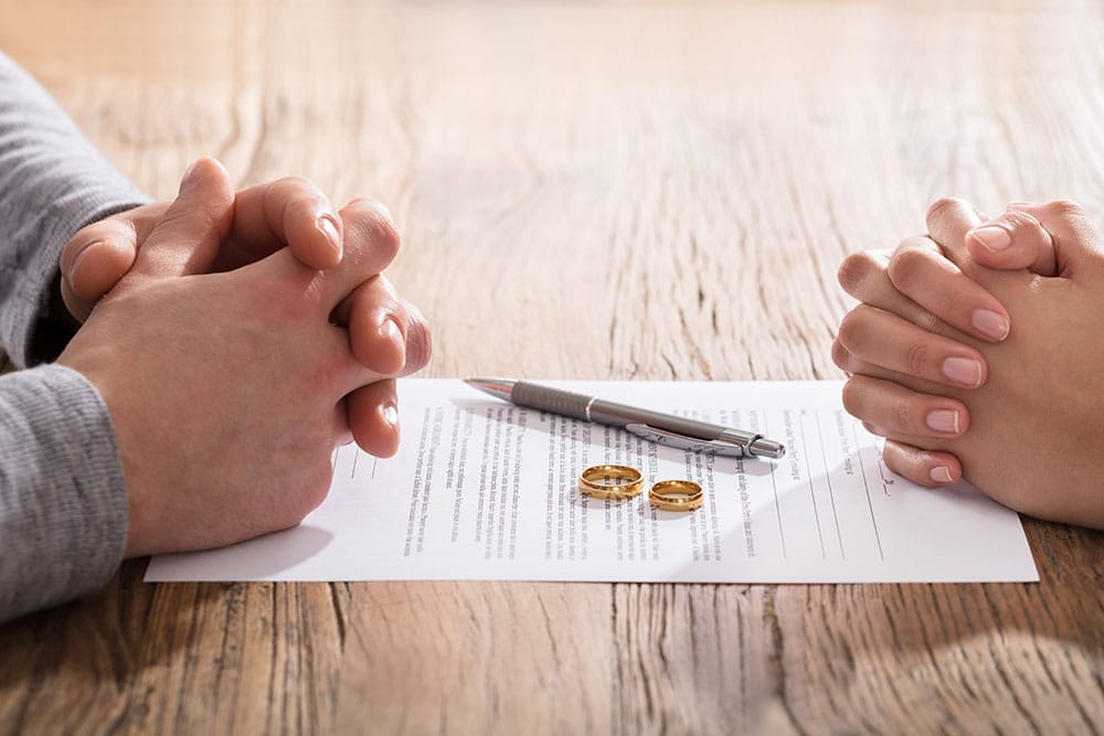 Hands Of Wife And Husband On Divorce Document With Wedding Ring In The Center