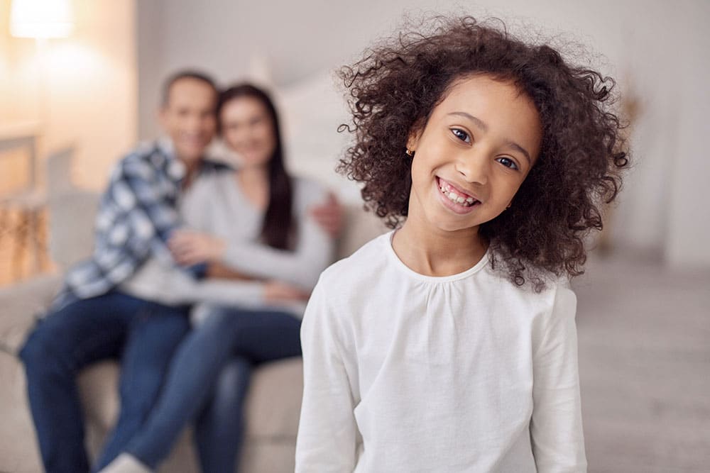 Happy life. Nice alert curly-haired girl smiling and her sitting on the couch and hugging in the background