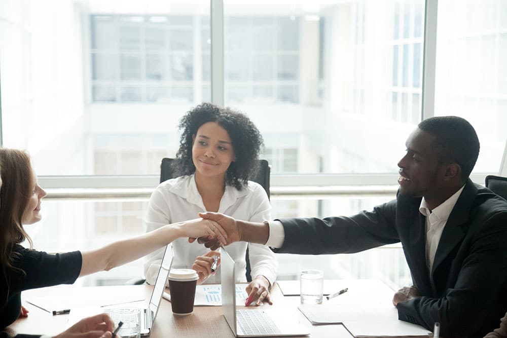 Smiling african businessman handshaking greeting caucasian businesswoman at group meeting negotiation, black satisfied entrepreneur welcoming partner shaking hand in lawyers office, respect concept