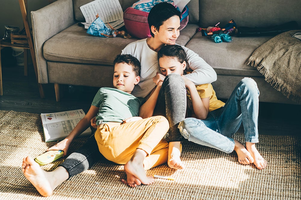 Happy mother hugs her children siblings on floor.