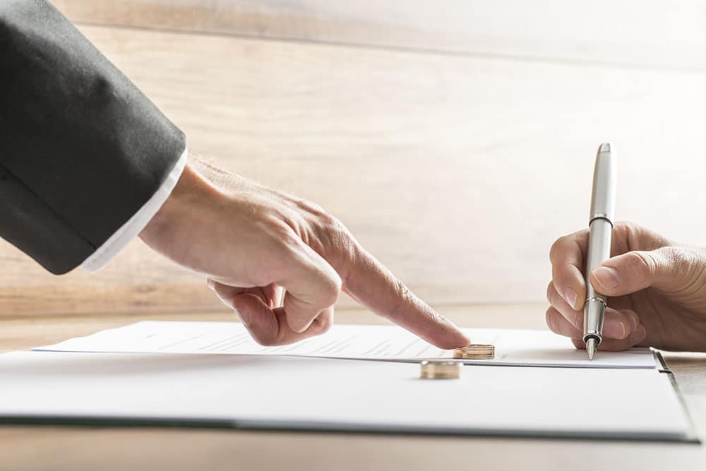 Male hand pushing a wedding ring over to a female hand about to sign divorce papers. Conceptual of divorce or marriage.