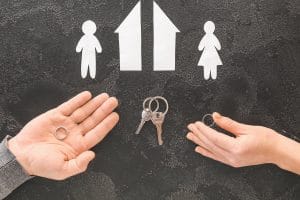 Male and female hands with wedding rings, keys, cut figures of house and couple on dark background. Concept of divorce