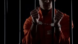 Prisoner in orange uniform showing handcuffs, looking angry and disappointed