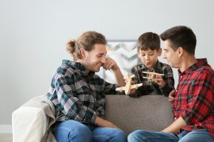 Happy gay couple playing with adopted child at home