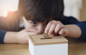 Blurry face of kid with thinking face putting 10 pence on money box, Selective focus little boy making stack British money coins and counting. Learning financial responsibility and saving for future