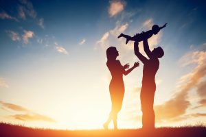 Happy family together, parents with their little child at sunset. Father raising baby up in the air.