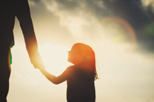 silhouette of little girl holding parent hand at sunset sky