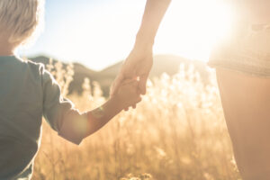 Mother little child holding hands walking in a grass field at su