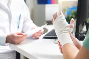 Injured patient showing doctor broken wrist and arm with bandage in hospital office or emergency room. Sprain, stress fracture or repetitive strain injury in hand. Nurse helping customer. First aid.