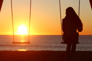 Single woman alone swinging on the beach and looking the other seat missing a boyfriend