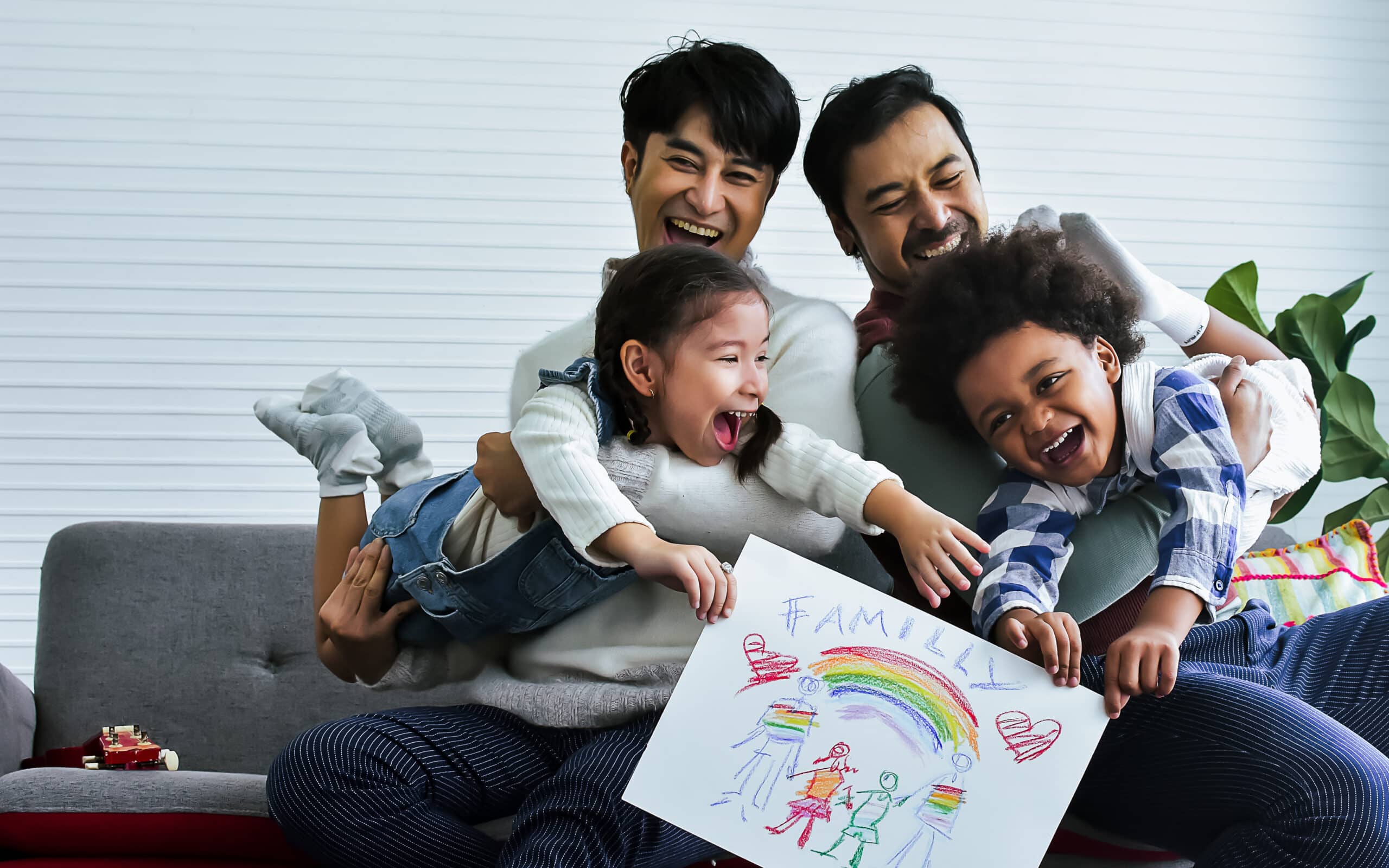 Male gay taking care adopted children who are happy diverse little Caucasian girl and African boy, playing with fun, drawing family picture, sitting on sofa in living room at home. LGBT, kids Concept