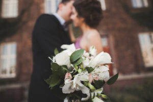Wedding flowers bouquet with newlywed couple on background.